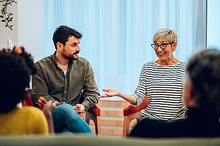 Personen unterschiedlichen Alters sitzen im Kreis, eine Person spricht und die anderen hören interessiert zu.